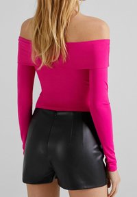 Tight passande långärmad topp i stark rosa med Off-shoulder halsringning, tillsammans med högmidjade svarta fusk lädershorts med dragkedja.