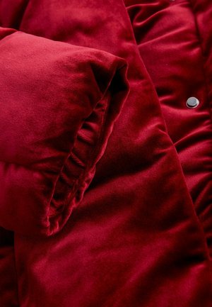 Piros bársonyos puffernadrág, puha textúrával, összegyűjtött ujjrész részletekkel és fényes patent gomb díszítéssel.