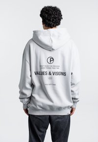 Felpa grigia chiaro realizzata in morbido tessuto. Presenta un grande cappuccio, polsini a costine e testo sul retro che include "VALORI E VISUALIZZAZIONI" in grassetto nero.