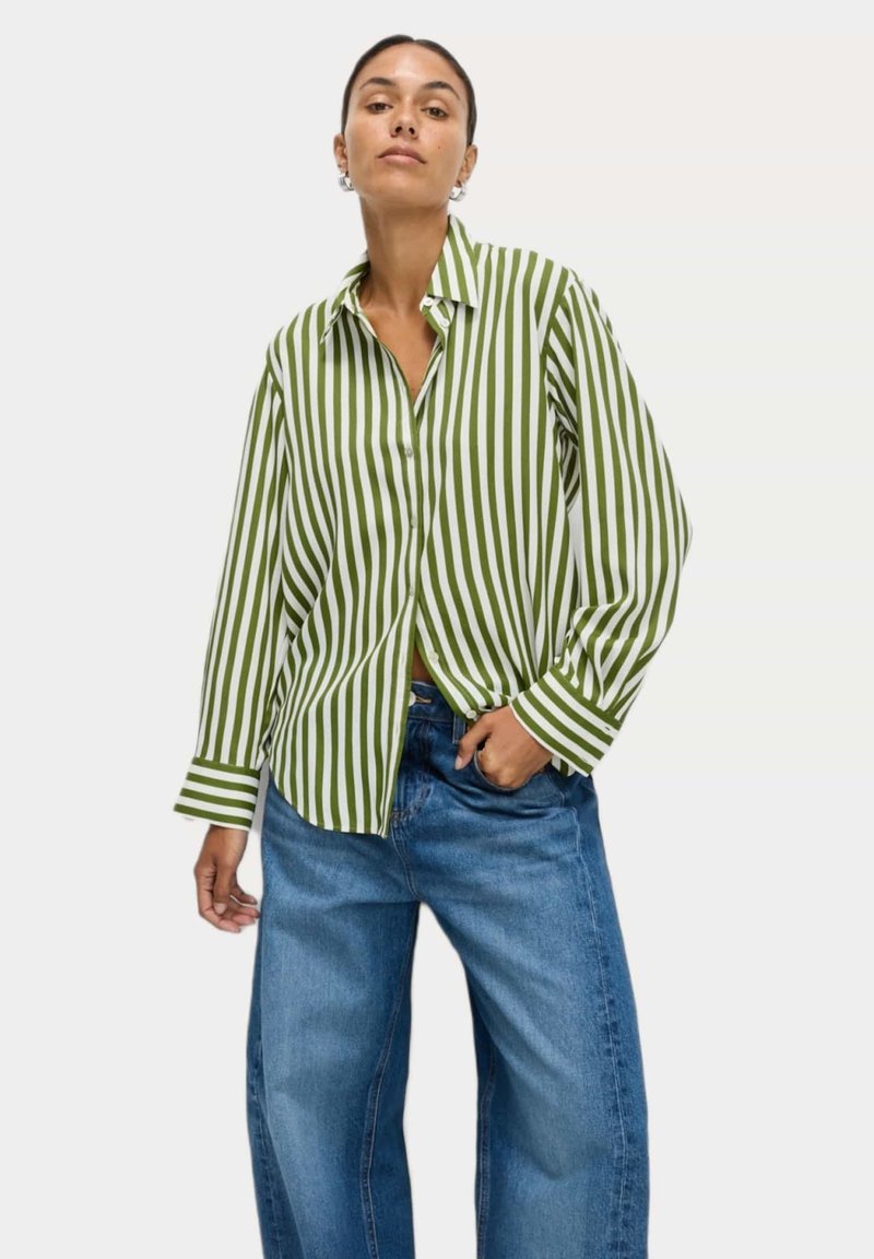 Camicia button-up a righe verdi e bianche con colletto, maniche lunghe e vestibilità rilassata, abbinata a jeans ampiflati blu.