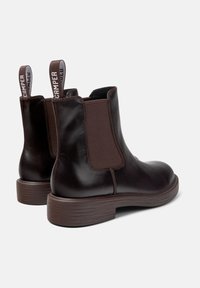 Bottes cheville en cuir marron avec panneaux élastiques sur les côtés et semelle en caoutchouc texturée. Présente un talon renforcé et une languette pour un enfilage facile.