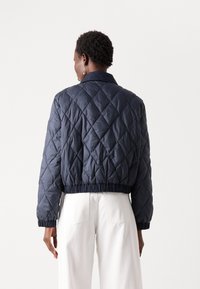 Marineblauwe gewatteerde pufferjack met een cropped ontwerp, ribgebreide manchetten en kraag. Heeft een elastische zoom en glanzende afwerking, geschikt voor casual draag.