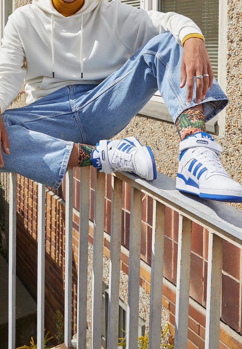 Vita högskor med blå accenter och tre ränder, kombinerat med färgglada mönstrade strumpor och avslappnade ljusblå jeans.