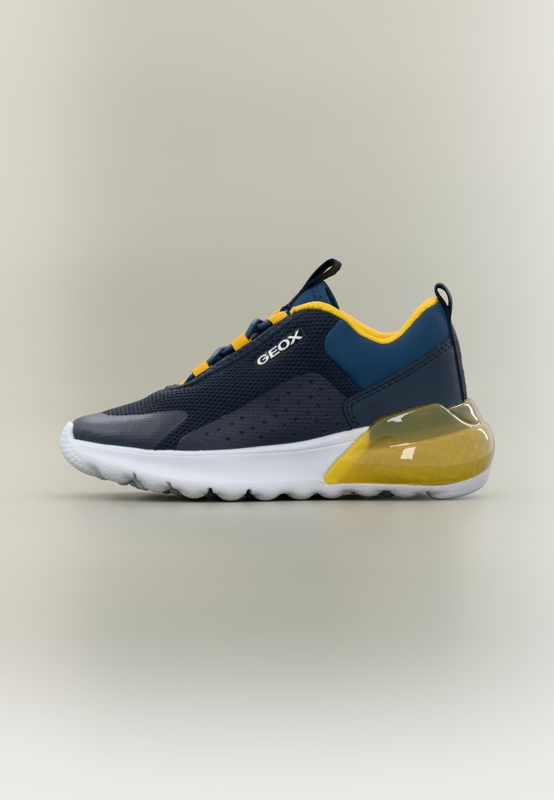Αθλητικό παπούτσι σε ναυτικό μπλε και κίτρινο με άσπρη σόλα, επάνω μέρος από διαπνέον πλέγμα, ταινίες για εύκολο φόρεμα και λογότυπο επωνυμίας στο πλάι, σε ουδέτερο φόντο.