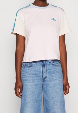 Osoba ubrana w biały krótki rękaw koszulki Adidas z niebieskimi paskami na ramionach oraz jasnoniebieskie dżinsy.