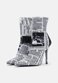 Stivaletti bianchi alla caviglia con stampa nera di giornale, punta affusolata, tacco a stiletto e chiusura con cerniera. Texture liscia con finitura lucida.