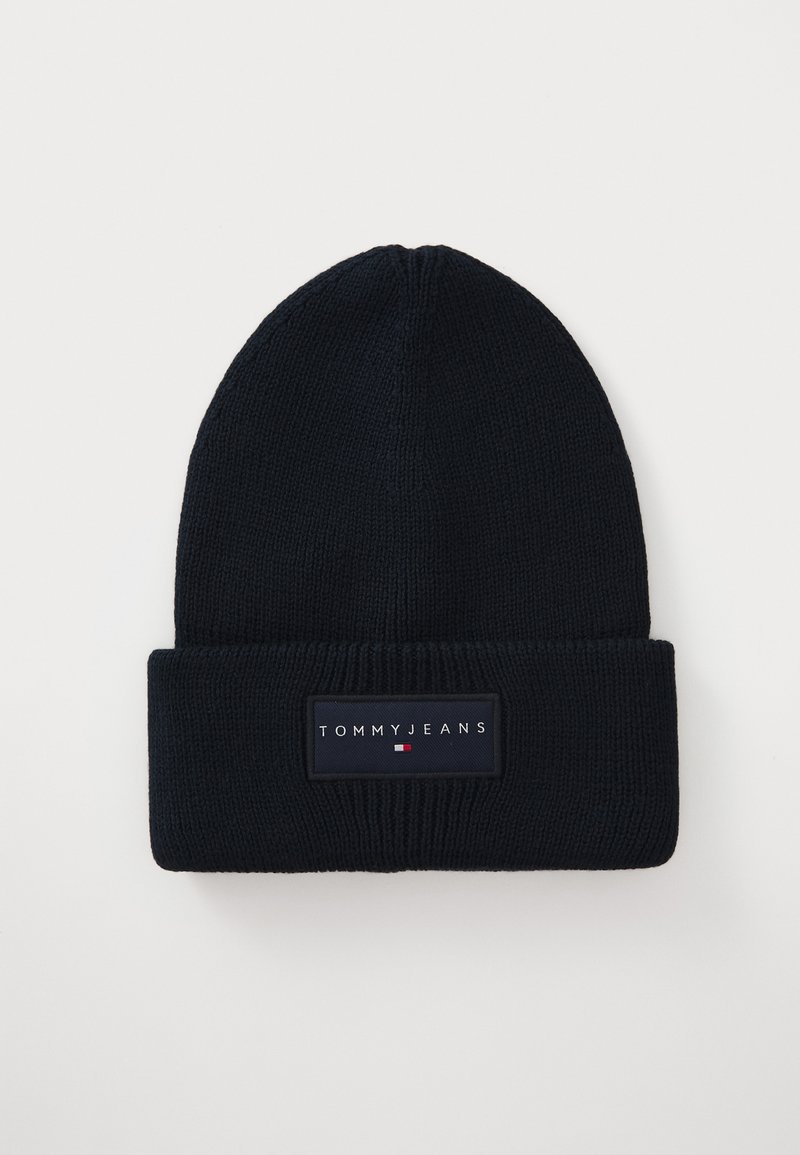 Navy knitted beanie with a folded cuff and prominent fabric label featuring the text "TOMMY JEANS" and a small tri-color graphic.