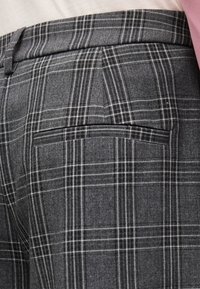 Κοντινό πλάνο σε γκρι καρό παντελόνι ραμμένο στα μέτρα με πίσω τσεπή, φορεμένο με λευκό πουκάμισο και ροζ σακάκι.