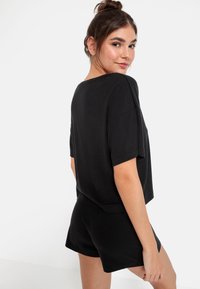 Svart ribbad kortärmad topp i kombination med matchande svarta shorts. Tyget verkar mjukt med en avslappnad passform och rundad halsringning.