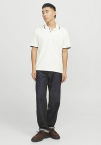 Valge polo särk, millel on mereväe ja punased aktsendid, koos tumedate denim pükstega. Pruunid lippsaad liistudega ja tekstureeritud tallaga. Igapäevane sobivus.