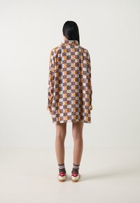 Skjortklänning med ett geometriskt mönster i orange och marinblått, långa ärmar och krage. Pairad med röda sneakers och bruna randiga strumpor.