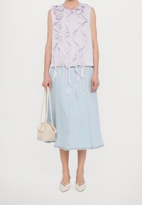 Kvinna som bär en ärmlös lavendelfärgad topp med volanger, en ljusblå midi-denimkjol, vita spetsiga skor och håller en liten vit vävd handväska.