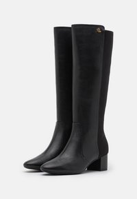 Bottes en cuir noir hauteur genoux avec une texture lisse, bout pointu et talon carré. Présentent un accent en logo doré en haut.