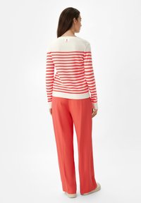 Rood-wit gestreepte trui met lange mouwen en een ronde halslijn; gecombineerd met koraalrode wijde broek. Zachte textuur, minimale details.