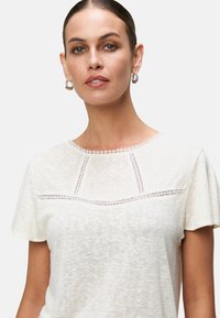 Crème korte mouwen t-shirt van textured stof, met ingewikkelde kantdetails langs de halslijn en de bovenste voorkant.