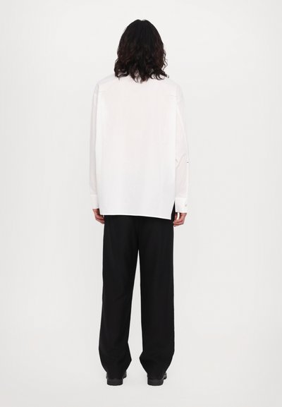 Chemise blanche à manches longues et coupe droite, assortie à un pantalon noir à jambes larges. Design simple sans motifs ni accents visibles.