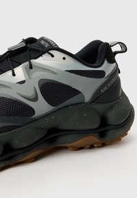 Black and gray sneaker with a textured mesh upper, rounded rubber sole, and prominent lacing system. Features Merrell branding on the heel.
