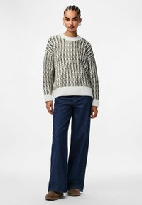 Pull en maille crème et vert olive avec un motif chaîne. Associé à un jean en denim foncé à jambes larges et à des chaussures marron sans lacets.