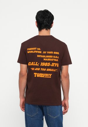 Ruda medvilnės marškinėliai su oranžiniu retro tekstu gale. Apatinėje dalyje yra frazės "FREIGHT CO." ir "TOMMY". Trumpomis rankovėmis, apvalios kaklo iškirptės dizainas.