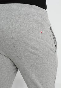 Pantalones de chándal grises que cuentan con un único bolsillo trasero con un pequeño detalle de logo rojo. Suave tejido texturizado que proporciona comodidad y flexibilidad.