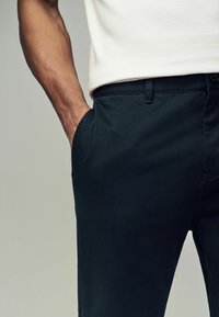 Sorte bomuldsblandede bukser med en tapered fit. Linningen har en knaplukning og sidelommer til nytte. Struktureret stof er synligt.