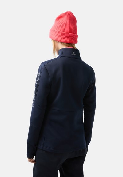 Navy fleece jacket with a high collar, featuring a logo on the back and text pattern on the right sleeve. Paired with a bright pink beanie.