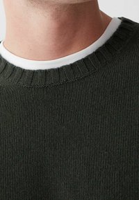 Tmavě zelený pletený svetr s žebrovaným kulatým výstřihem a bílým vnitřním límcem. Textura vypadá měkká a hustě tkaná.