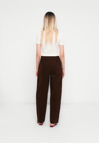 Bruine wijde corduroy-broek met een zachte textuur, gecombineerd met een aansluitend wit kort mouwtopje, gezien van achteren. Rode sandalen zichtbaar.