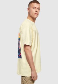 Camiseta de algodón amarilla con mangas cortas y un corte relax. Presenta una colorida impresión gráfica en la parte posterior, que muestra figuras abstractas.