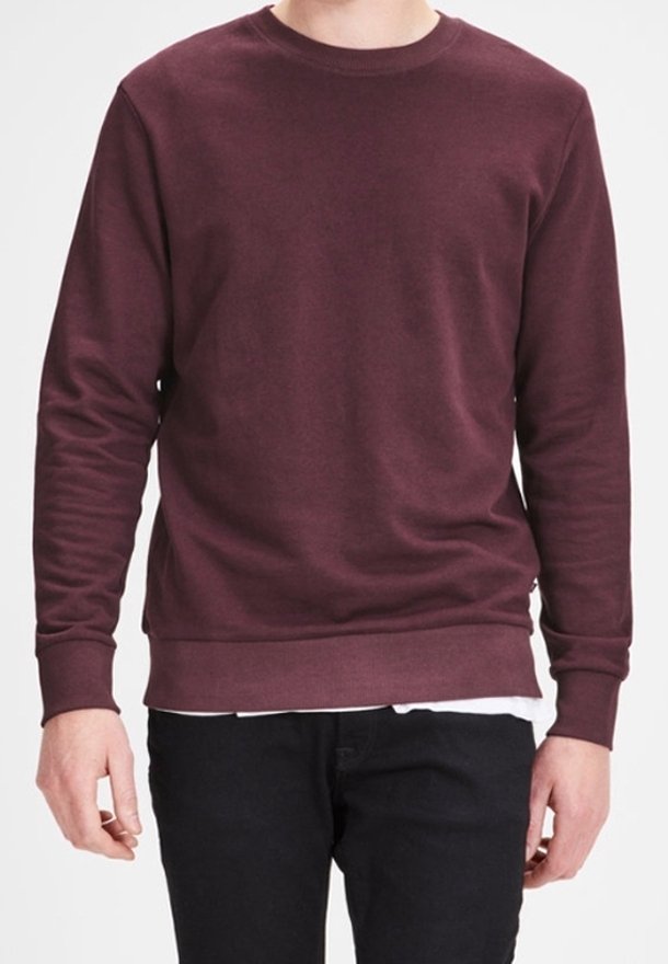 Bordeauxrode sweatshirt van zachte stof met lange mouwen, ronde hals en geribbelde zoom. Gedragen over een wit overhemd, gecombineerd met donkere jeans.