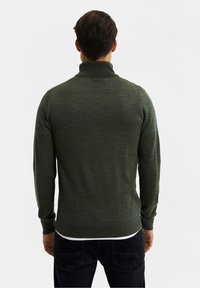 Maglione aderente verde scuro con collo alto e maniche lunghe, realizzato in un tessuto morbido. I polsini e l'orlo a coste conferiscono struttura.