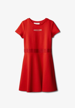 Rode katoenen jurk met korte mouwen, ronde hals en een getailleerde taille. Voorzien van een contrasterende tailleband en een logo op de borst. Zwarte schoenen.
