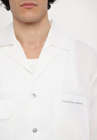 Weißes Hemd mit Knopfleiste und glänzender Oberfläche, Brusttasche sowie besticktem "Feng Chen Wang", ausgestattet mit einem lässigen Kragen und weichem Material.