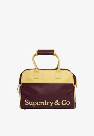 Rechthoekige kastanjebruine en gele leren tas met handvatten en "Superdry & Co" gedrukt in grote gele letters op het voorpaneel.