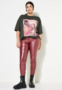 Olijfgroen oversized t-shirt met een roze printontwerp, gecombineerd met strakke bordeauxkleurige faux leren broeken en zwarte laarzen met een dikke zool.