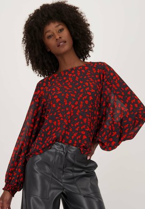 Blouse florale rouge en tissu transparent, fond noir, manches larges et coupe décontractée, assortie à un pantalon taille haute en simili cuir noir.