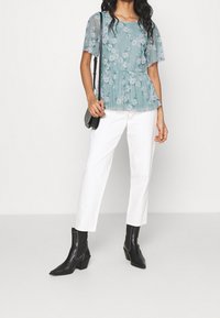 Světle modrý květinový top s krátkými rukávy, designem peplum, spárovaný s bílými kalhotami a černými kotníkovými botami. Plochá kožená taška přes rameno.