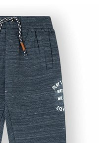 Pantalones de chándal grises hechos de una tela texturizada. Cuentan con una cintura de canalé, cordón ajustable y texto impreso en blanco en una pierna.