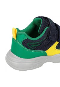 Baskets colorées avec un design vert et jaune, en tissu bleu foncé texturé, avec une sangle ajustable et un col rembourré.