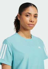 T-shirt de sport bleu clair en tissu texturé, avec trois rayures blanches sur chaque manche et un petit logo blanc sur la poitrine.