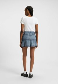 Witte, aansluitende T-shirt en een blauwe spijkerrok met rafelige zoom, voorzien van gelaagde ruches en een ceintuur in de taille, gecombineerd met zwarte schoenen en witte sokken.