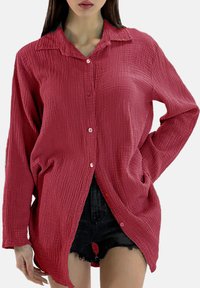 Krøllet bordeaux skjorte med krave, lange ærmer og knapper foran. Stoffet har en tekstureret finish med en løs og afslappet pasform.