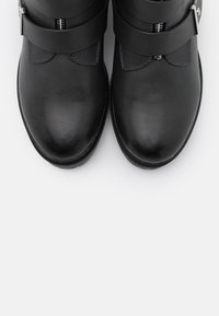 Botas de tobillo de cuero negro con un acabado suave, que cuentan con una cremallera frontal y dos correas anchas con acentos metálicos.
