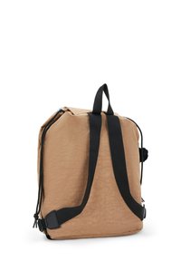 Mochila de tela color beige con correas negras, forma rectangular, superficie texturada, que cuenta con un cierre de cordón y un pequeño detalle de pompones.