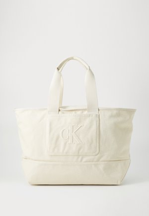 Platnena torba u krem boji, s dva platnena ručka. Sadrži utisnuti logo na prednjem zakrpu. Jednostavan dizajn, strukturiran oblik.