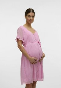Roza, pokrivna majica za trudnice s točkicama, kratkim volanastim rukavima, v-izrezom, prednjim dugmadima i remenom, osmišljena za udobnost i dostupnost.