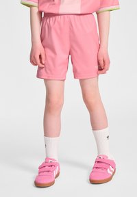 Rosa idrottsshorts gjorda av ett lättviktsmaterial med resårmidja, bärs tillsammans med vita strumpor och rosa sneakers med kardborreband.