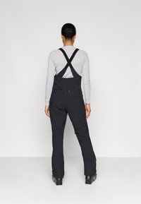 Salopete de schi negre, fabricate dintr-un material durabil, cu bretele reglabile, o croială ajustată și buzunare laterale.