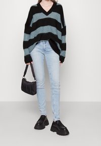 Striped oversized sweater in black and teal, V-neck design, paired with light blue skinny jeans and chunky black lace-up shoes.