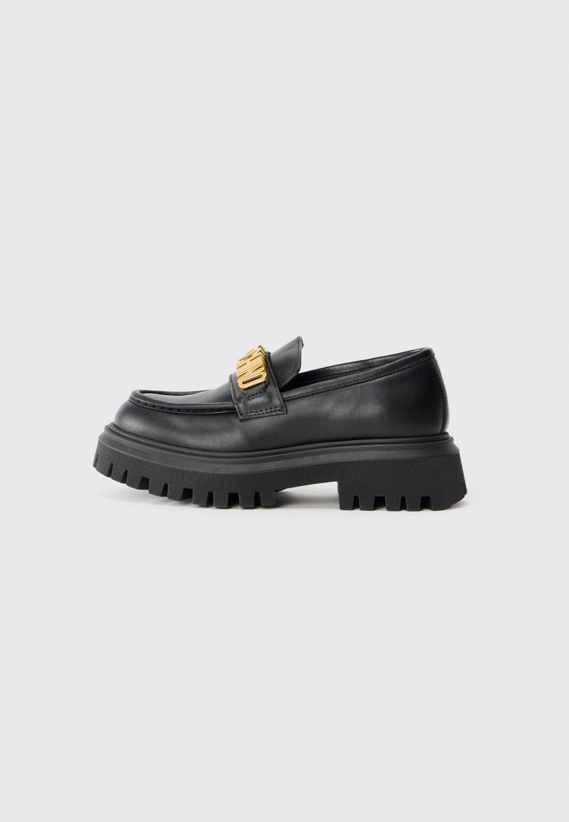 Svarta läder loafers med en kraftig gummisula, med en gyllene detalj på ovandelen och en rundad tådesign.